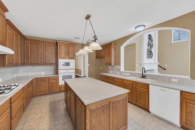 kitchen featuring white appliances, a kitchen island, light countertops, and a sink