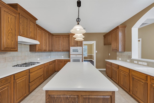 kitchen featuring brown cabinetry, white appliances, and under cabinet range hood