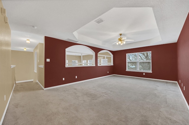 empty room featuring visible vents, a tray ceiling, and baseboards