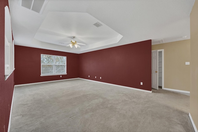 unfurnished room with visible vents, a tray ceiling, carpet, and attic access