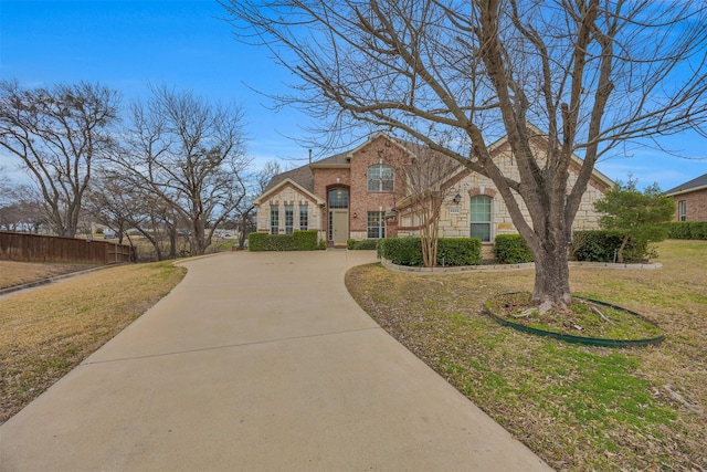 view of front of home featuring brick siding, fence, stone siding, driveway, and a front lawn