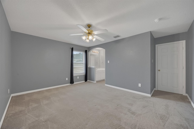 unfurnished bedroom with visible vents, arched walkways, baseboards, and light colored carpet