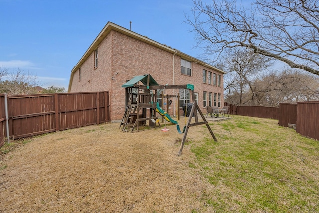 back of house with brick siding, a lawn, a playground, and a fenced backyard