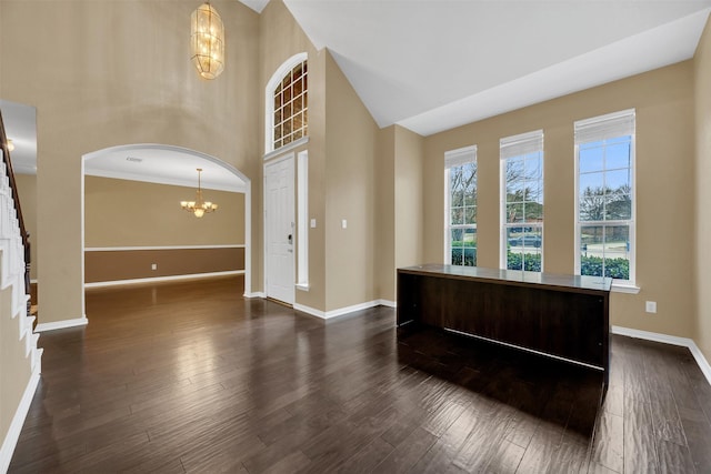 interior space featuring baseboards, arched walkways, dark wood finished floors, a high ceiling, and a notable chandelier