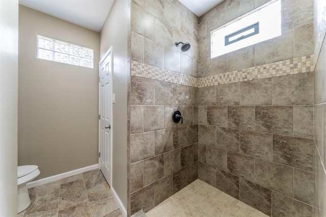 bathroom featuring stone finish flooring, tiled shower, toilet, and baseboards