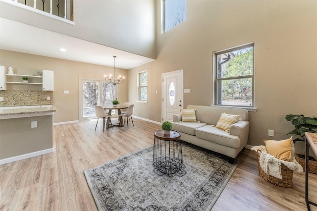 living area featuring light wood-type flooring, a towering ceiling, baseboards, and a notable chandelier