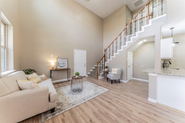 living room with baseboards, visible vents, stairway, a high ceiling, and light wood-type flooring