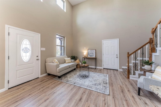 foyer entrance featuring a high ceiling, baseboards, stairway, and light wood finished floors