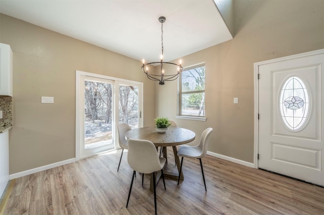 dining area featuring light wood-type flooring, a notable chandelier, and baseboards