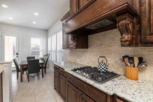 kitchen with light tile patterned floors, dark brown cabinets, backsplash, and stainless steel gas stovetop