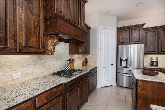 kitchen featuring light tile patterned floors, stainless steel appliances, backsplash, dark brown cabinetry, and light stone countertops