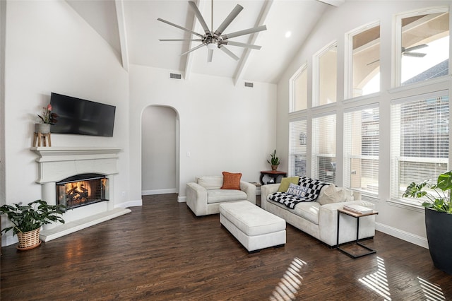 living area featuring arched walkways, ceiling fan, a warm lit fireplace, visible vents, and dark wood-style floors