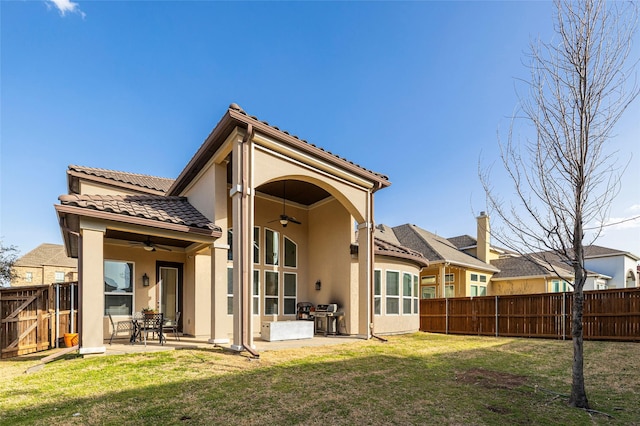 rear view of house with ceiling fan, a tiled roof, a fenced backyard, and stucco siding