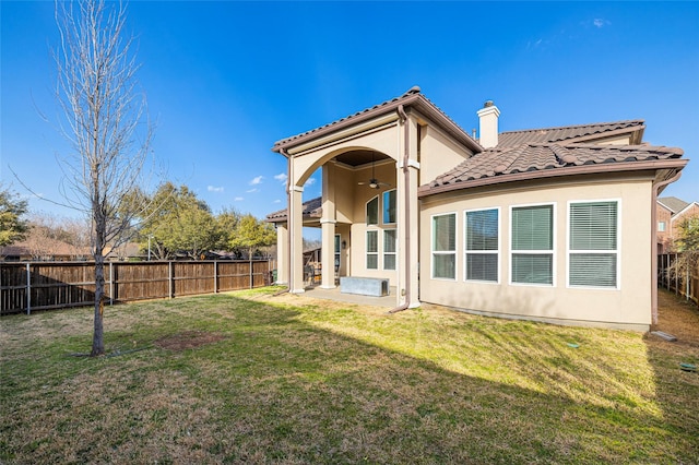 rear view of house with ceiling fan, a fenced backyard, a tile roof, a lawn, and a chimney