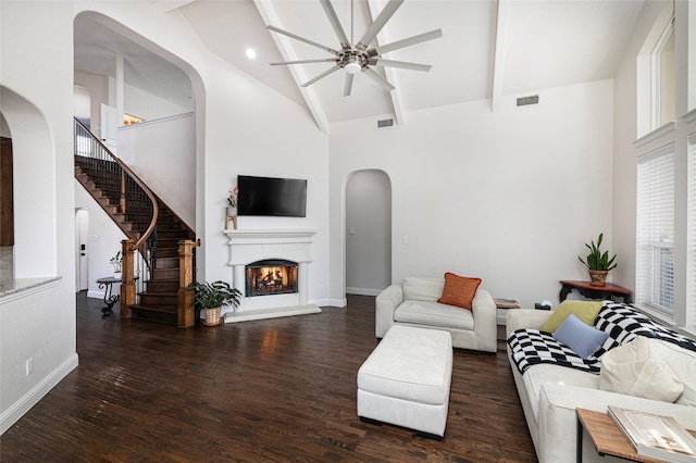 living room featuring visible vents, wood finished floors, high vaulted ceiling, a warm lit fireplace, and beamed ceiling