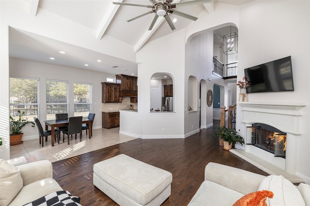 living room featuring arched walkways, wood finished floors, beamed ceiling, and a glass covered fireplace