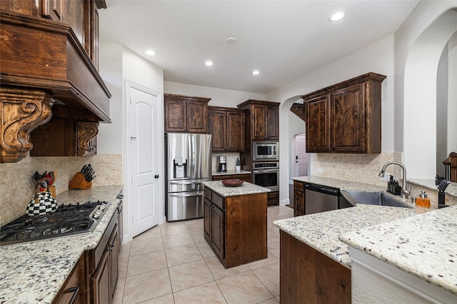 kitchen featuring dark brown cabinetry, arched walkways, appliances with stainless steel finishes, light stone countertops, and a sink