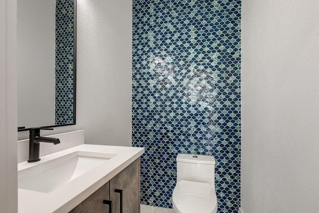 half bath with toilet, a textured wall, and vanity