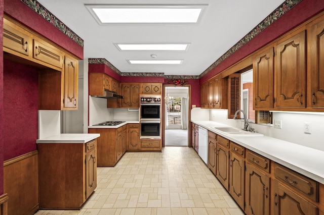 kitchen featuring dishwasher, electric stovetop, multiple ovens, under cabinet range hood, and a sink