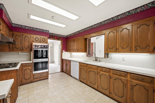 kitchen with brown cabinets, black electric stovetop, light countertops, a sink, and dishwasher