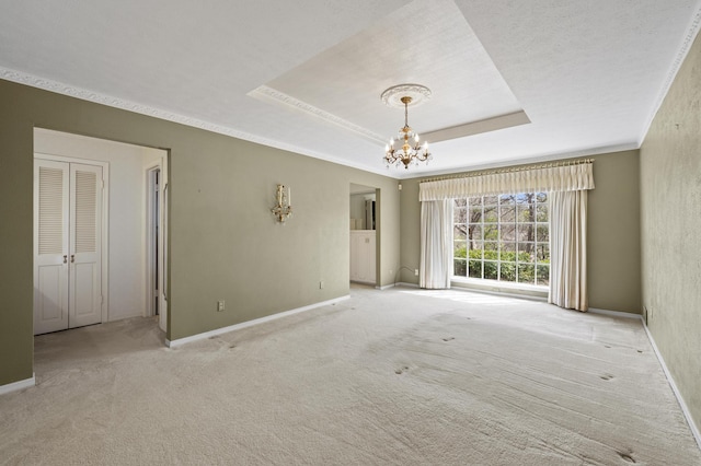 carpeted spare room with an inviting chandelier, baseboards, a tray ceiling, and crown molding