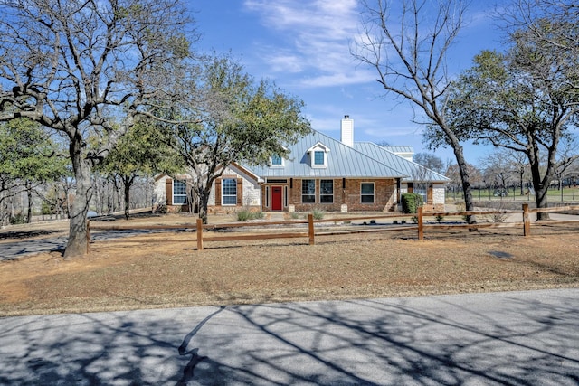 view of front facade featuring metal roof, a fenced front yard, a chimney, and a standing seam roof