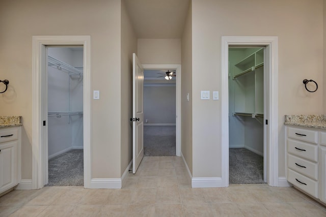 full bath featuring tile patterned flooring, vanity, a walk in closet, and baseboards