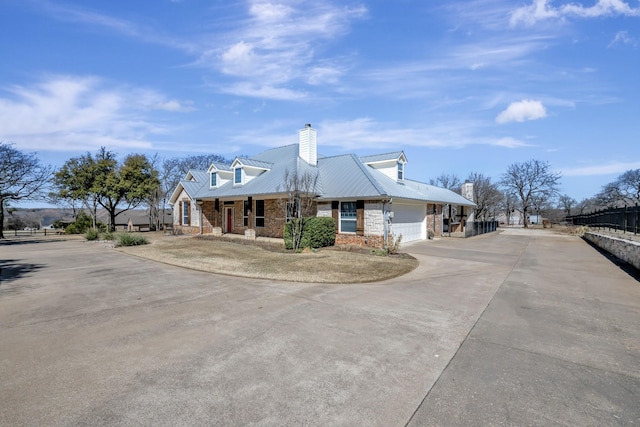 view of front of home featuring stone siding, concrete driveway, an attached garage, metal roof, and a chimney