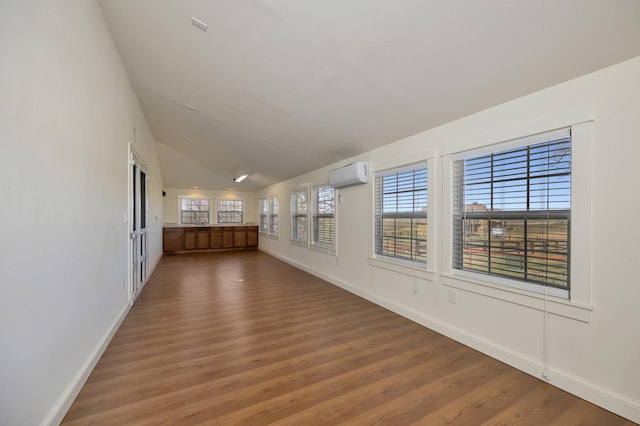 unfurnished room featuring a wall unit AC, wood finished floors, baseboards, and vaulted ceiling