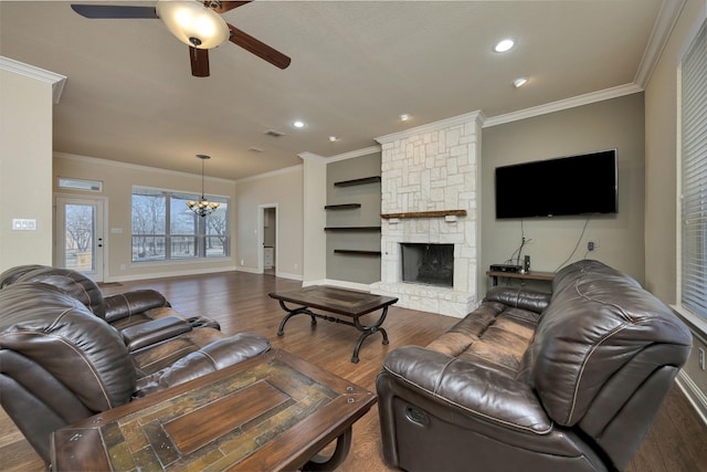 living room with visible vents, crown molding, ceiling fan with notable chandelier, a fireplace, and wood finished floors