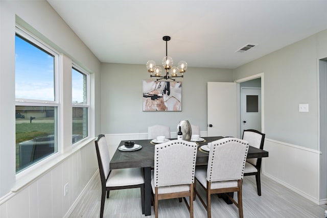 dining area with a wainscoted wall, light wood-style flooring, visible vents, and a notable chandelier