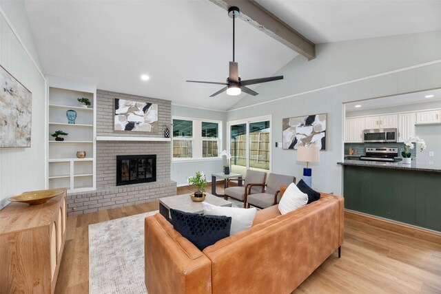 living area featuring lofted ceiling with beams, a brick fireplace, light wood-type flooring, and ceiling fan