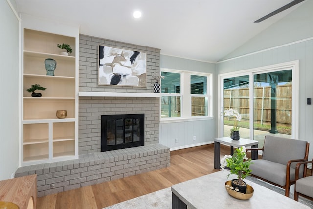 living room featuring vaulted ceiling, built in shelves, a brick fireplace, and wood finished floors