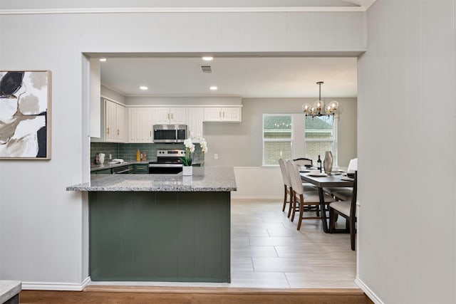 kitchen featuring visible vents, appliances with stainless steel finishes, a peninsula, white cabinetry, and backsplash