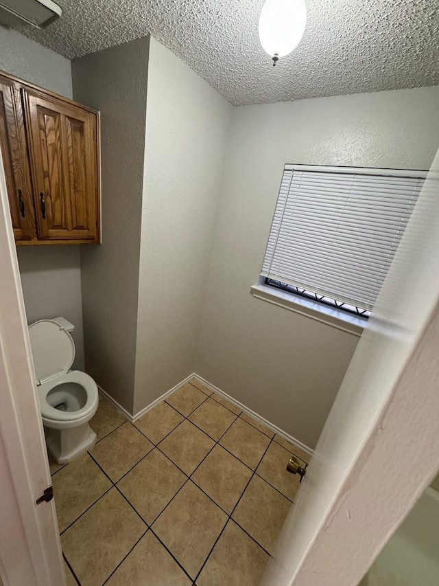 bathroom featuring baseboards, toilet, a textured wall, tile patterned floors, and a textured ceiling