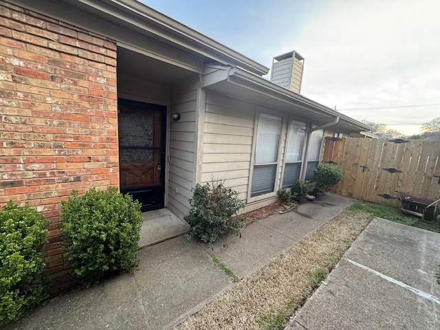 doorway to property featuring fence, brick siding, and a chimney