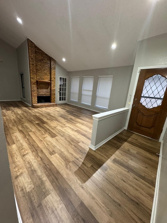 entrance foyer featuring a brick fireplace, vaulted ceiling, recessed lighting, wood finished floors, and a textured ceiling