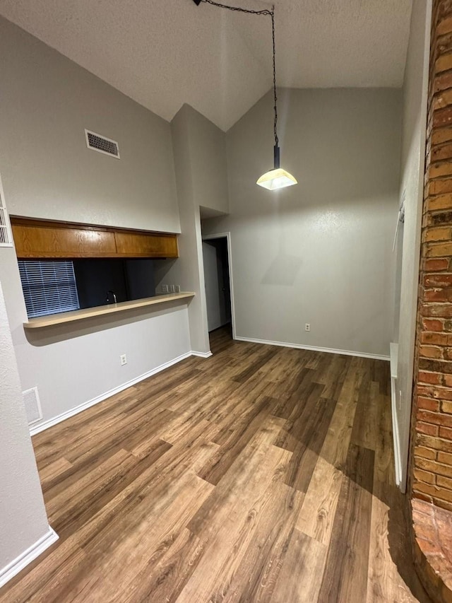 interior space featuring visible vents, baseboards, lofted ceiling, wood finished floors, and a textured ceiling