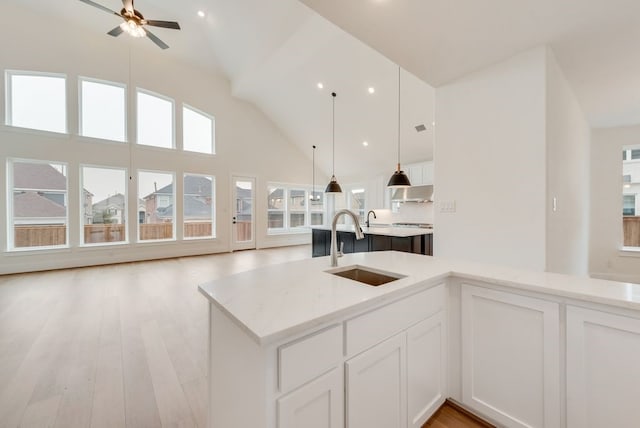 kitchen with decorative light fixtures, light wood-style floors, white cabinetry, high vaulted ceiling, and a sink