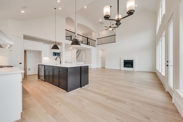 kitchen with high vaulted ceiling, a fireplace, light countertops, stainless steel dishwasher, and light wood-type flooring