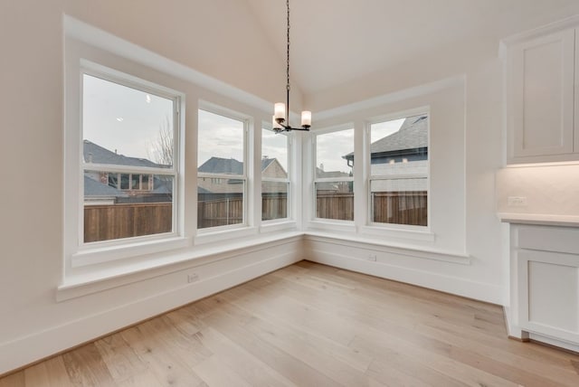 unfurnished dining area with lofted ceiling, light wood finished floors, baseboards, and a notable chandelier