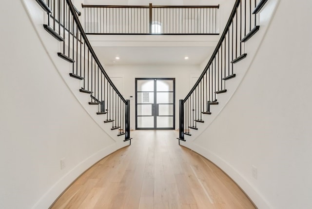 foyer with light wood finished floors, a high ceiling, and baseboards