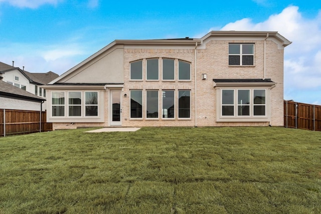 rear view of property with a fenced backyard, a lawn, and brick siding