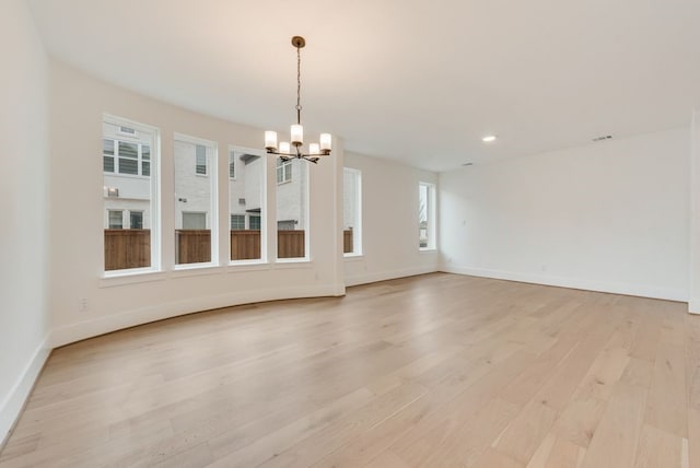 spare room with a chandelier, light wood-style flooring, and baseboards