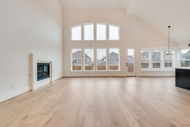 unfurnished living room with high vaulted ceiling, a glass covered fireplace, a notable chandelier, and light wood-style flooring