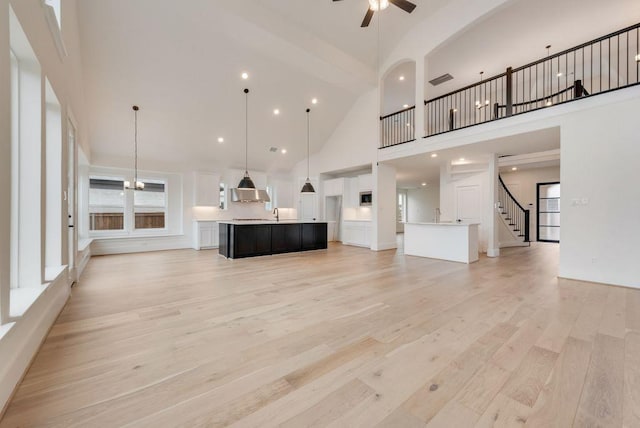 unfurnished living room featuring light wood finished floors, ceiling fan, stairway, a high ceiling, and recessed lighting