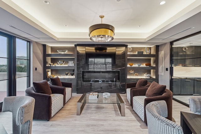 sitting room featuring light wood-type flooring, a high end fireplace, a raised ceiling, and recessed lighting