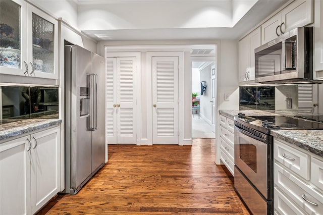 kitchen with light stone counters, glass insert cabinets, dark wood-style flooring, stainless steel appliances, and white cabinetry