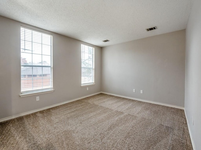 carpeted spare room with baseboards, visible vents, and a textured ceiling