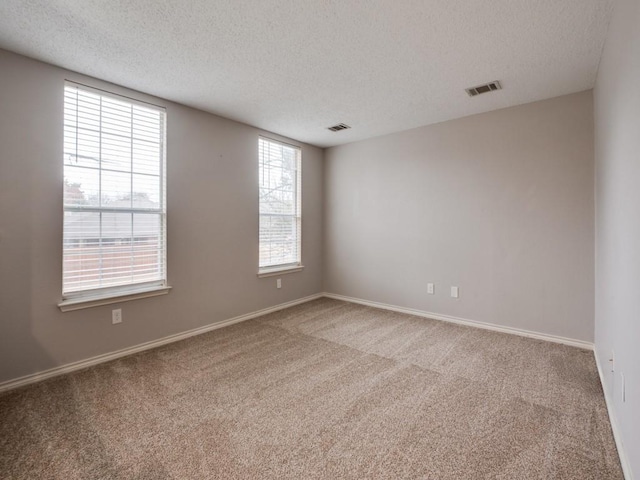 carpeted spare room with a textured ceiling, visible vents, and baseboards